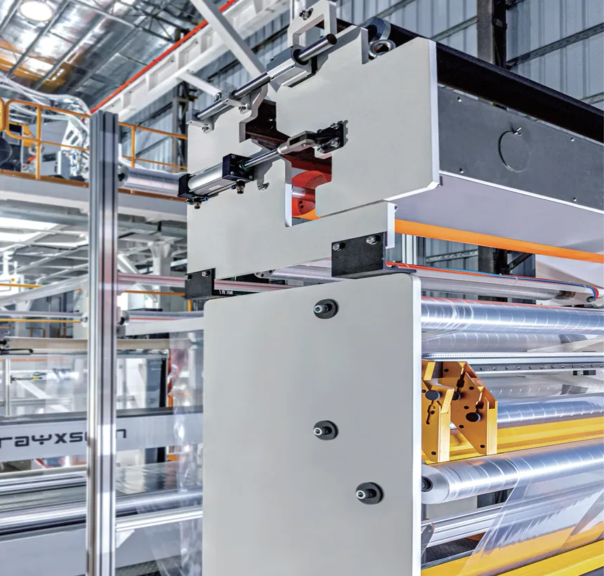Close-up of the control cabinet and swing-arm touchscreen mount on a blown film line, film web running over the rollers behind it